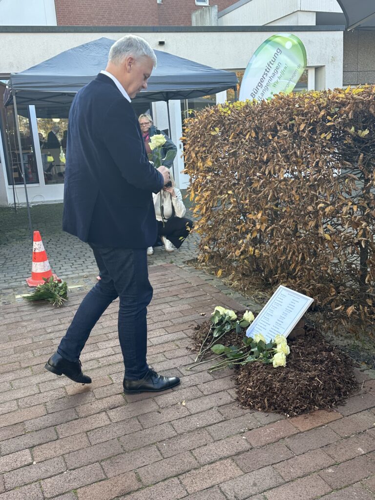 Bürgermeister Mirko Heuer legt eine Rose an der Stolperschwelle im Eichenpark nieder.